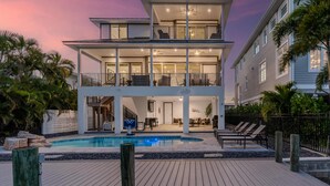 Una casa de dos pisos con piscina, mobiliario exterior y un balcón.