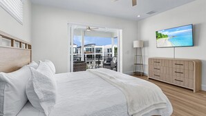 Un dormitorio con cama, televisor en la pared, ventilador de techo y vistas al balcón exterior.