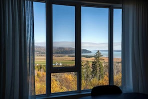 A room with a large window offering a view of a landscape with trees and a body of water.