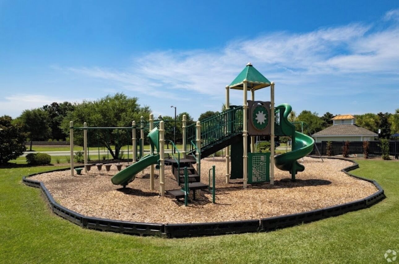 A playground with a green slide, a climbing structure, and a small shelter with a clock.