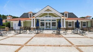 Un bâtiment doté d’une entrée centrale, d’un espace extérieur aménagé avec des tables et des chaises, et d’une terrasse couverte avec des parasols.