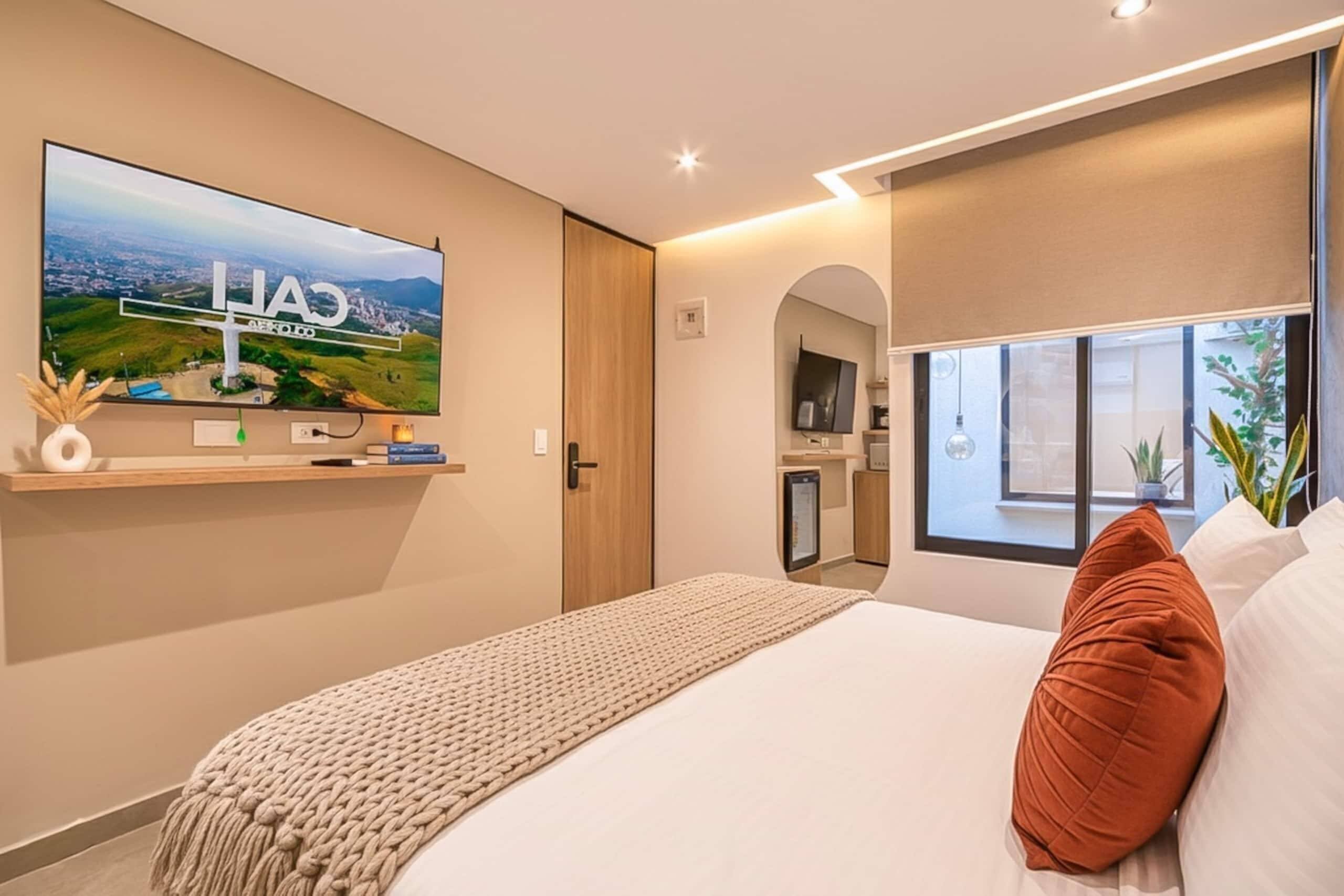Une chambre d’hôtel moderne avec un grand lit, un téléviseur fixé au mur et une vue sur le paysage urbain.