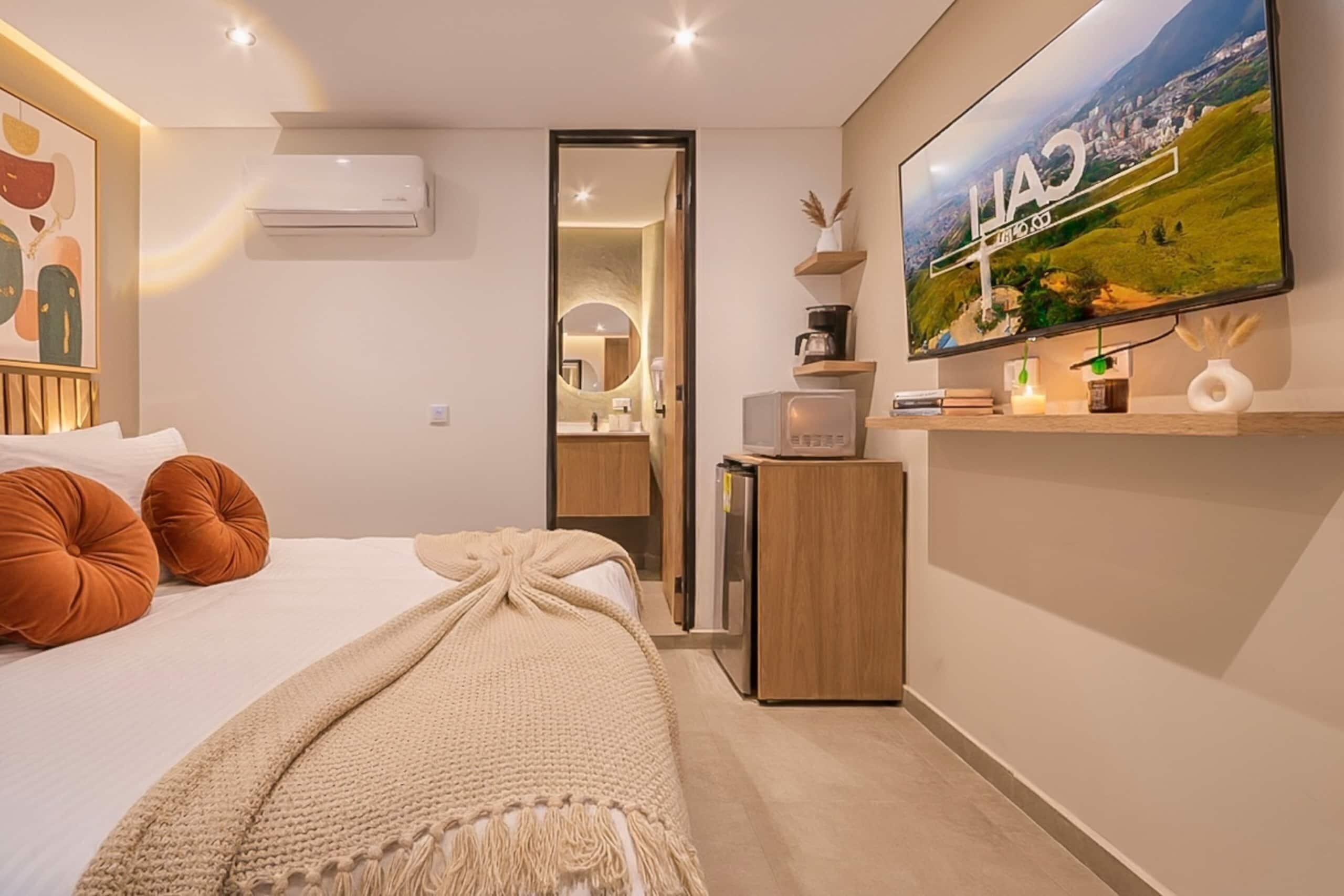 A modern bedroom with a bed, pillows, a TV, and a desk with a computer.
