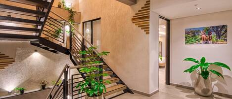 Un interior moderno con una escalera en espiral, una planta grande en maceta y un cuadro en la pared.