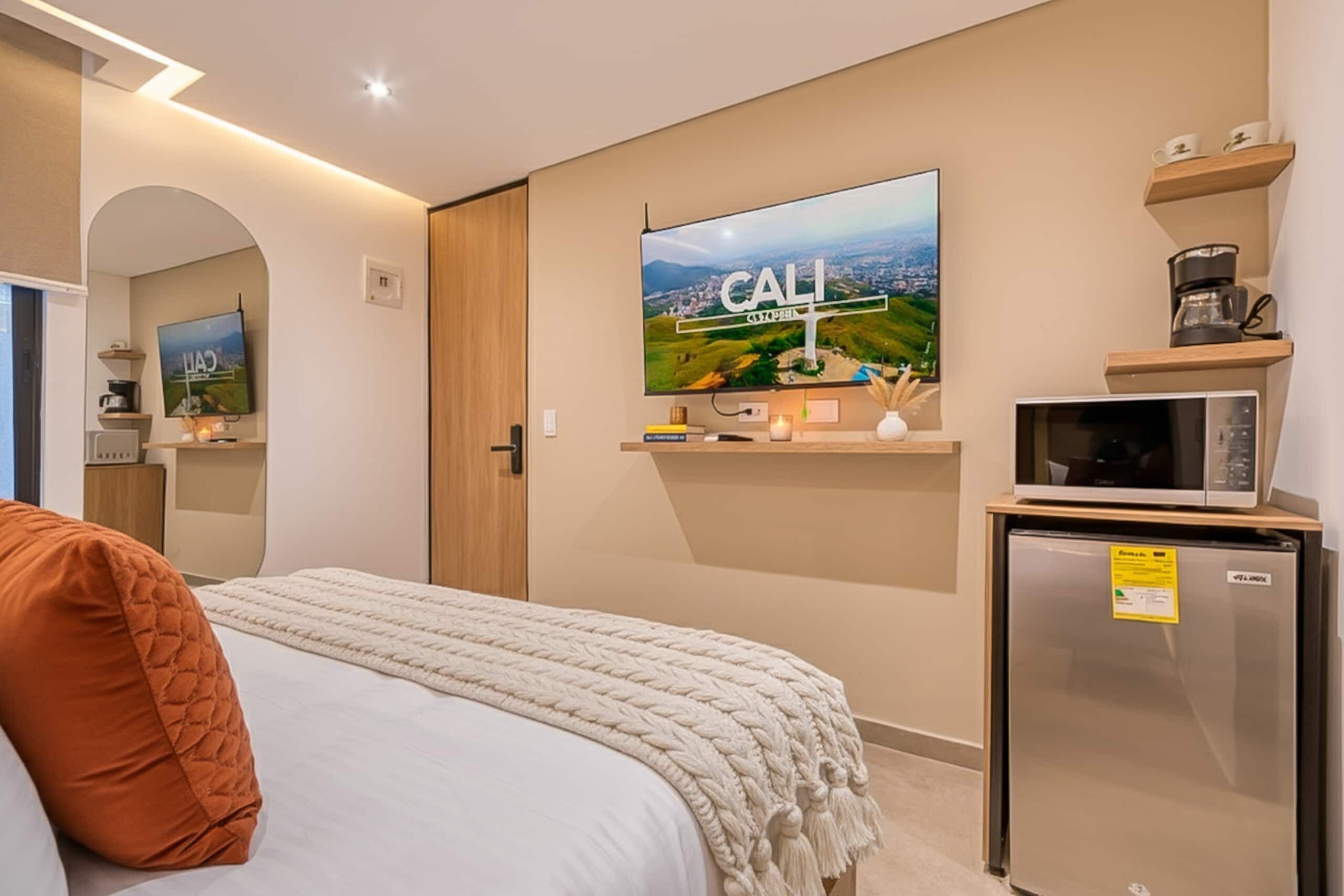 A hotel room with a bed, a TV mounted on the wall, a microwave, and a refrigerator.