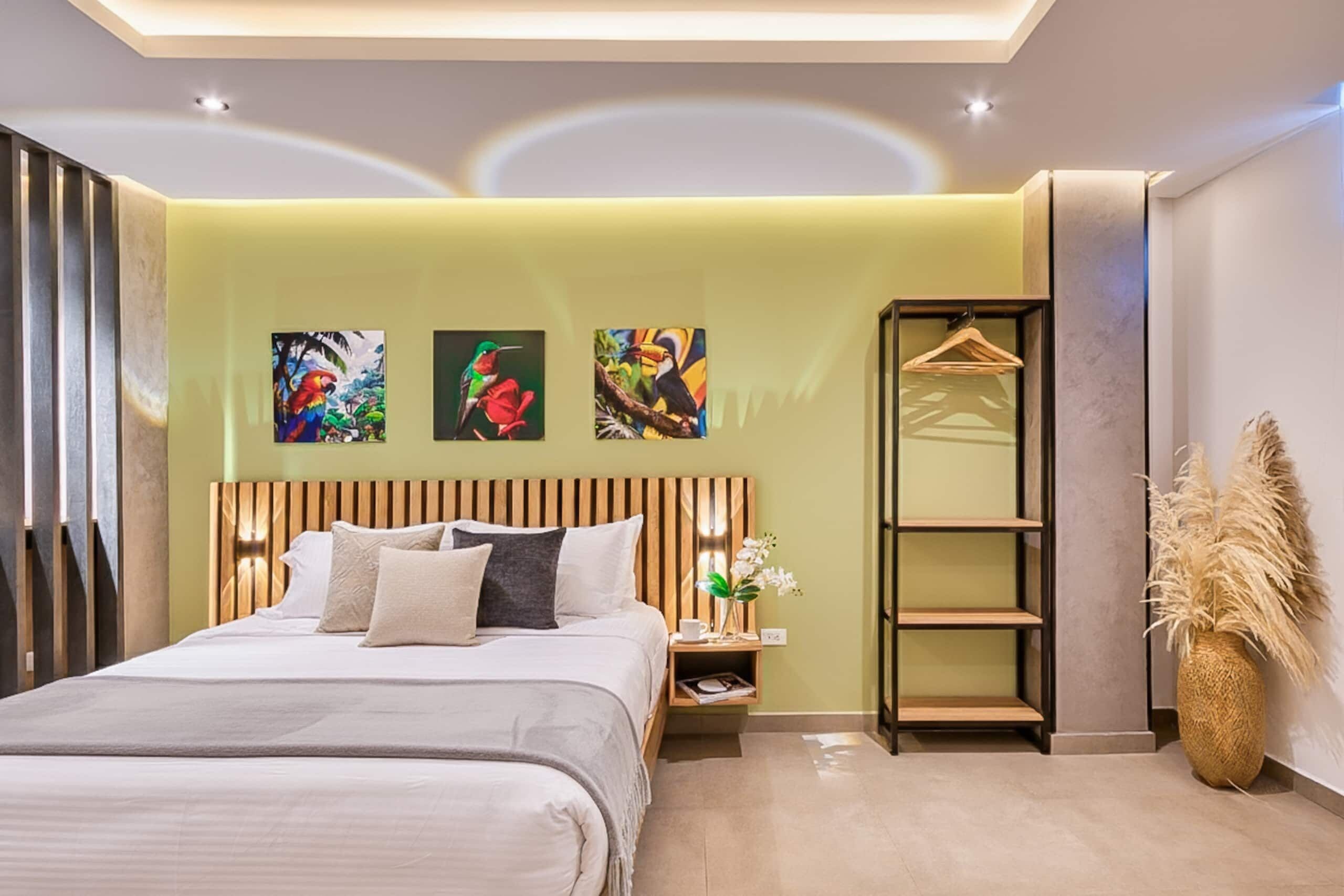 Une chambre à coucher moderne avec un lit, une table de chevet, une plante suspendue et des œuvres d’art accrochées au mur.