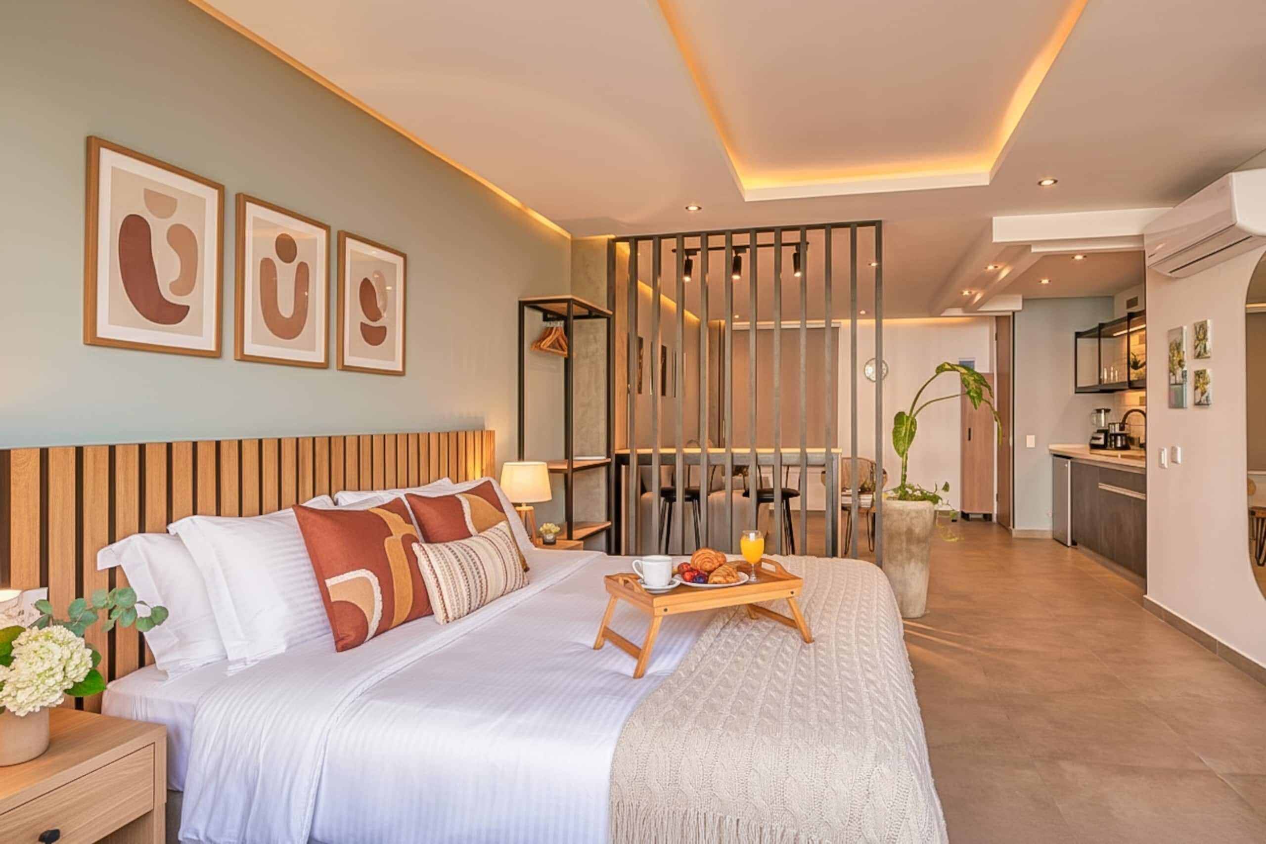 Una moderna camera d'hotel con un letto grande, comodini, una testiera in legno, una zona pranzo con tavolo e sedie, e un angolo cottura.