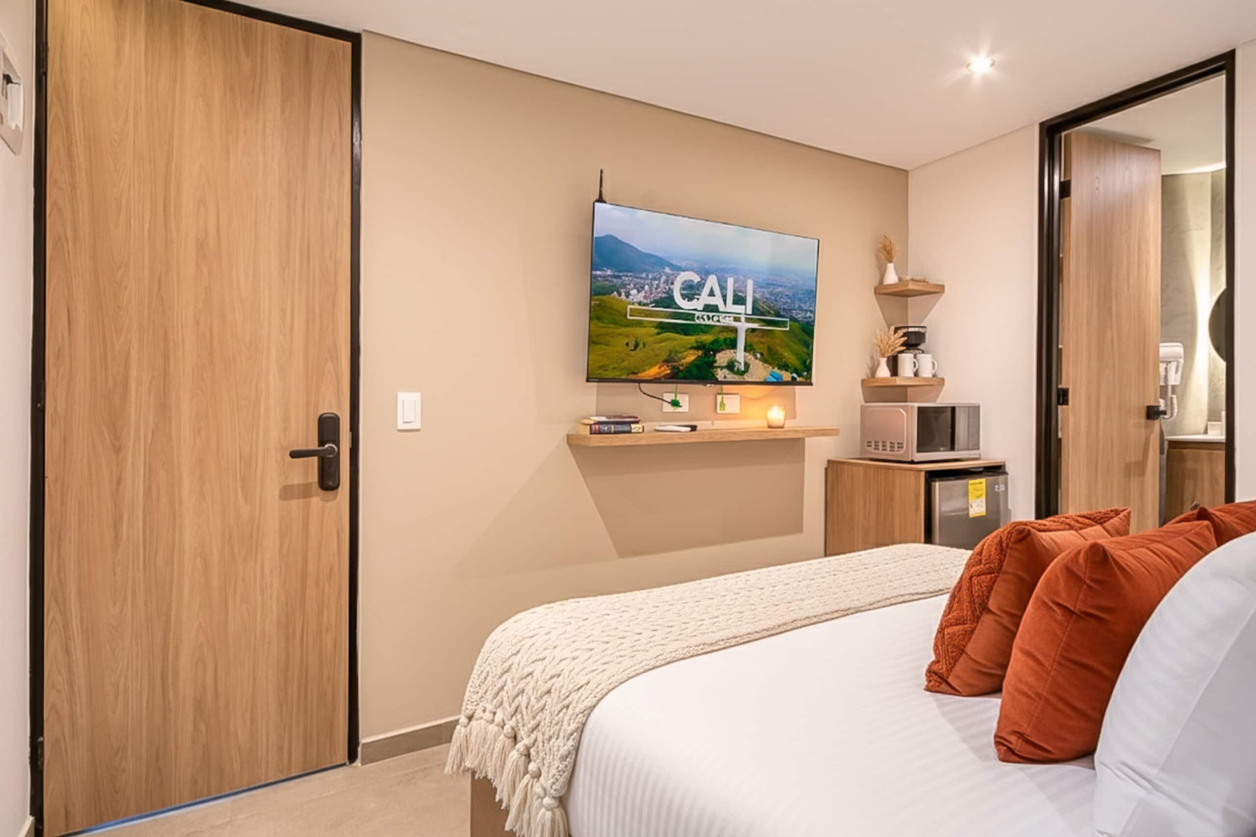 A hotel room with a bed, a television mounted on the wall, a microwave, and a small refrigerator.
