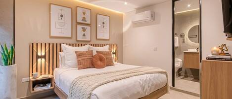 Un dormitorio moderno con una cama grande, mesitas de noche, aire acondicionado en la pared y obras de arte enmarcadas.