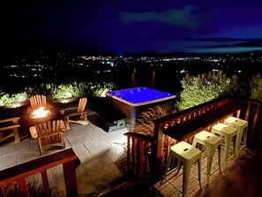 An outdoor patio area with a hot tub, seating, and a view of a cityscape at night. - Ultimate Winery Getaway - Private Hot Tub (Temecula)