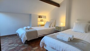 Une chambre d’hôtel avec deux lits, chacun équipé de draps et de serviettes blancs, une table de chevet avec une lampe et un sol carrelé.