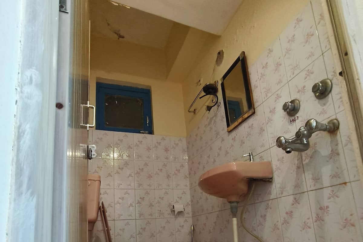 A bathroom with a toilet, sink, shower, and a red bucket.