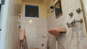 Casa de banho com sanita, lavatório, chuveiro e um balde vermelho.