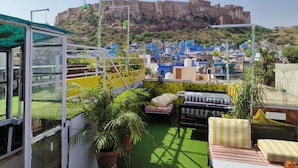Terraço no telhado com vista para uma fortaleza histórica, grama sintética verde e área de estar com almofadas.