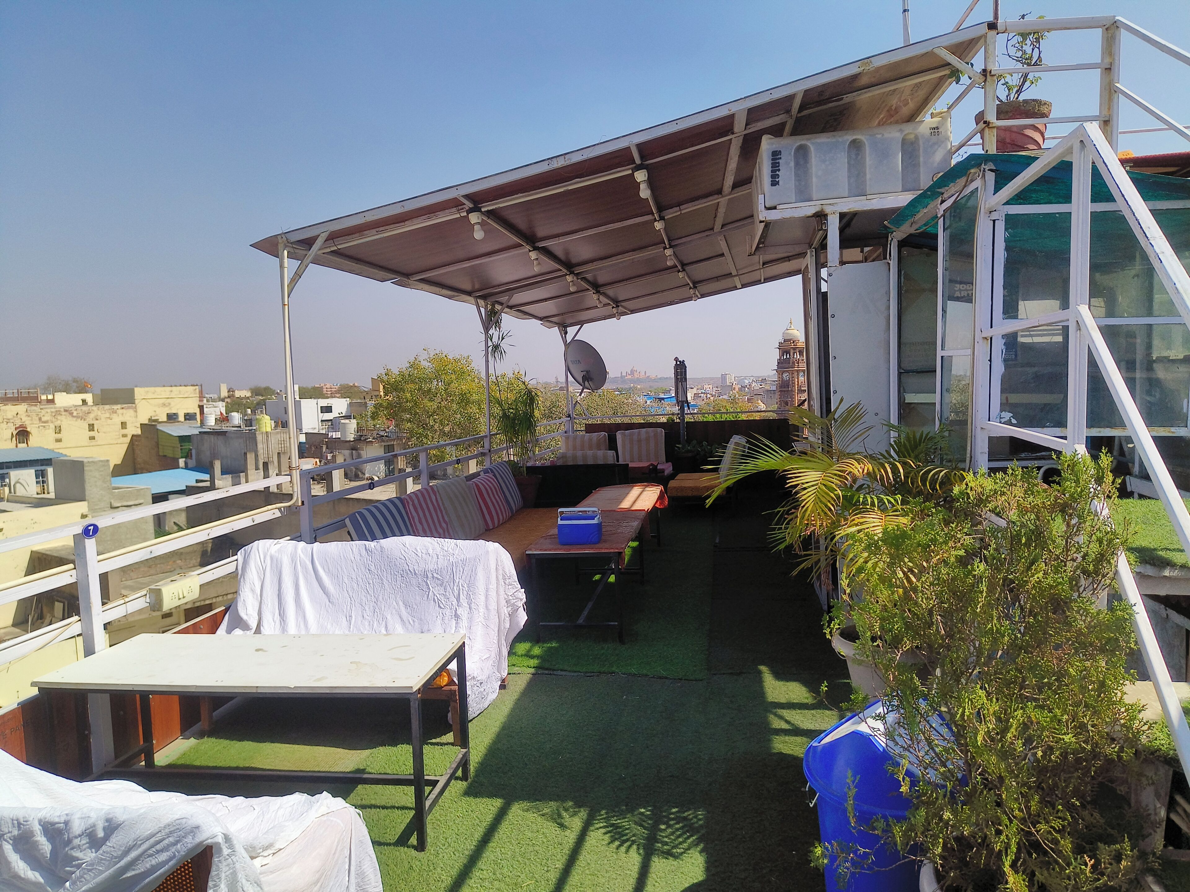 A rooftop terrace with a covered seating area, a table, and potted plants.