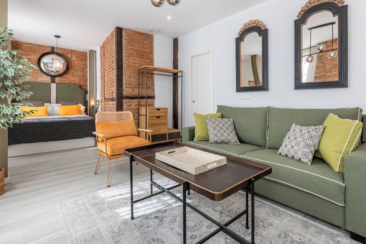 A modern living room with a green sofa, a wooden coffee table, and a brick accent wall.