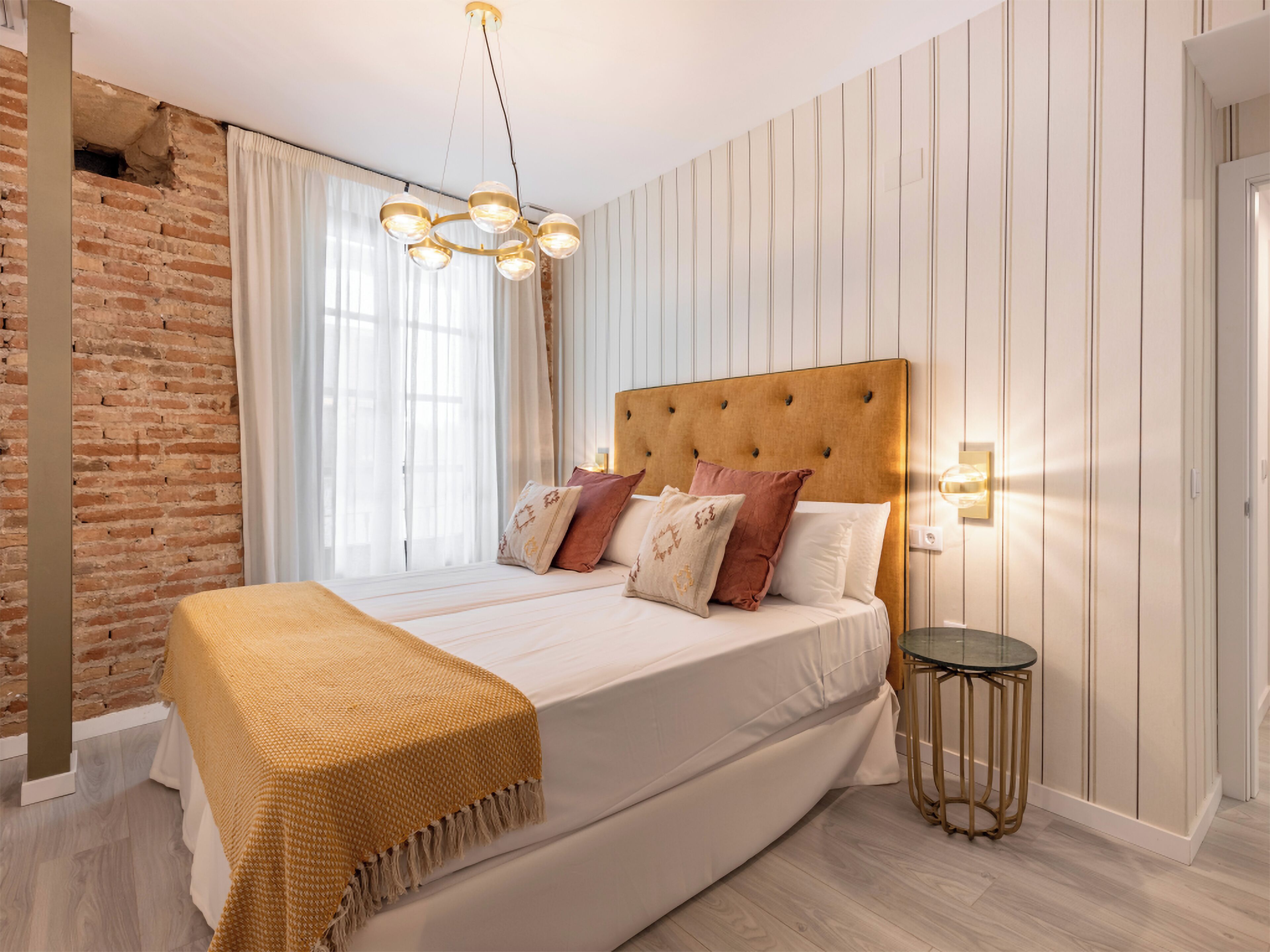 A bedroom with a brick wall, a large bed with a wooden headboard, and a glass table.