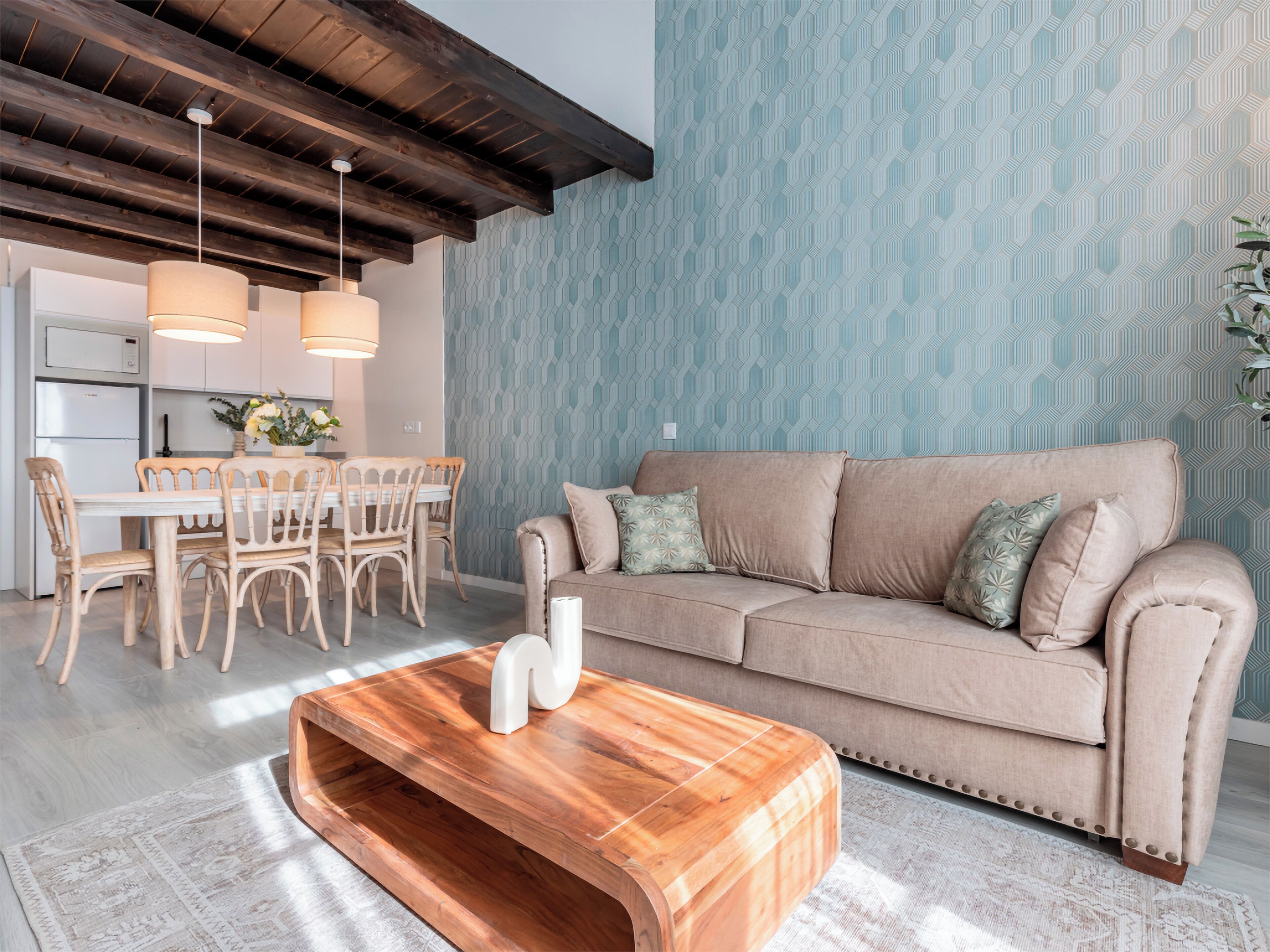 Un salon moderne avec une table basse en bois, un canapé beige et un papier peint à motifs.