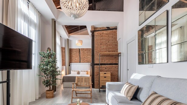 Un salon moderne avec un canapé gris, un téléviseur à écran plat, une table basse en bois agrémentée d’une plante et un mur en briques.