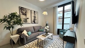 Un salon moderne avec un canapé gris, une table basse, un tapis à motifs, une plante en pot et des œuvres d’art accrochées au mur.