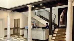 Un hall d’hôtel avec un sol à carreaux, un comptoir d’accueil, un escalier et des colonnes.