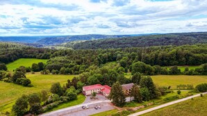 An aerial view of a rural property with a large building, surrounded by green fields and forests.