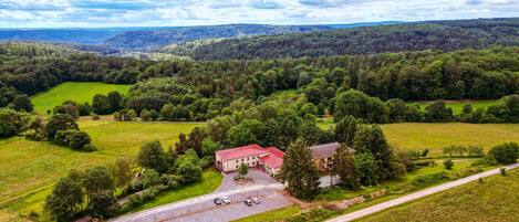 An aerial view of a rural property with a large building, surrounded by green fields and forests.