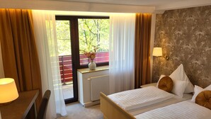 A hotel room with two beds, a desk with a lamp, a window with curtains, and a radiator.