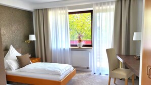 A hotel room with a bed, a desk, a chair, and a window with curtains.