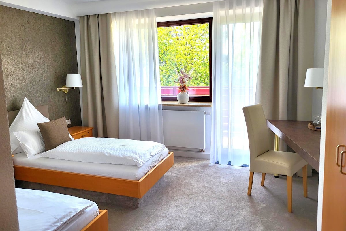 A hotel room with a bed, a desk, a chair, and a window with curtains.