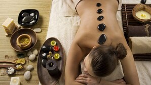 A person receiving a back massage with stones and candles on a massage table.