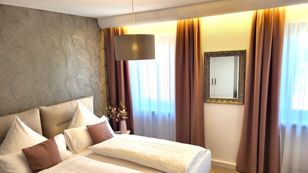 A hotel room with a large bed, a nightstand, a vase with flowers, a mirror, and curtains.
