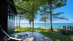Un terrazzo in legno con tavolo e sedie, affacciato su un’area verde con alberi e vista sul mare.