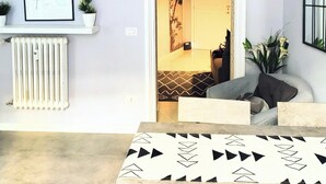 A modern living room with a sofa, a patterned table, a radiator, a framed picture, and a doorway leading to another room.