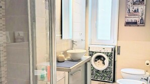 A modern bathroom with a glass shower enclosure, a sink, a toilet, and a washing machine.