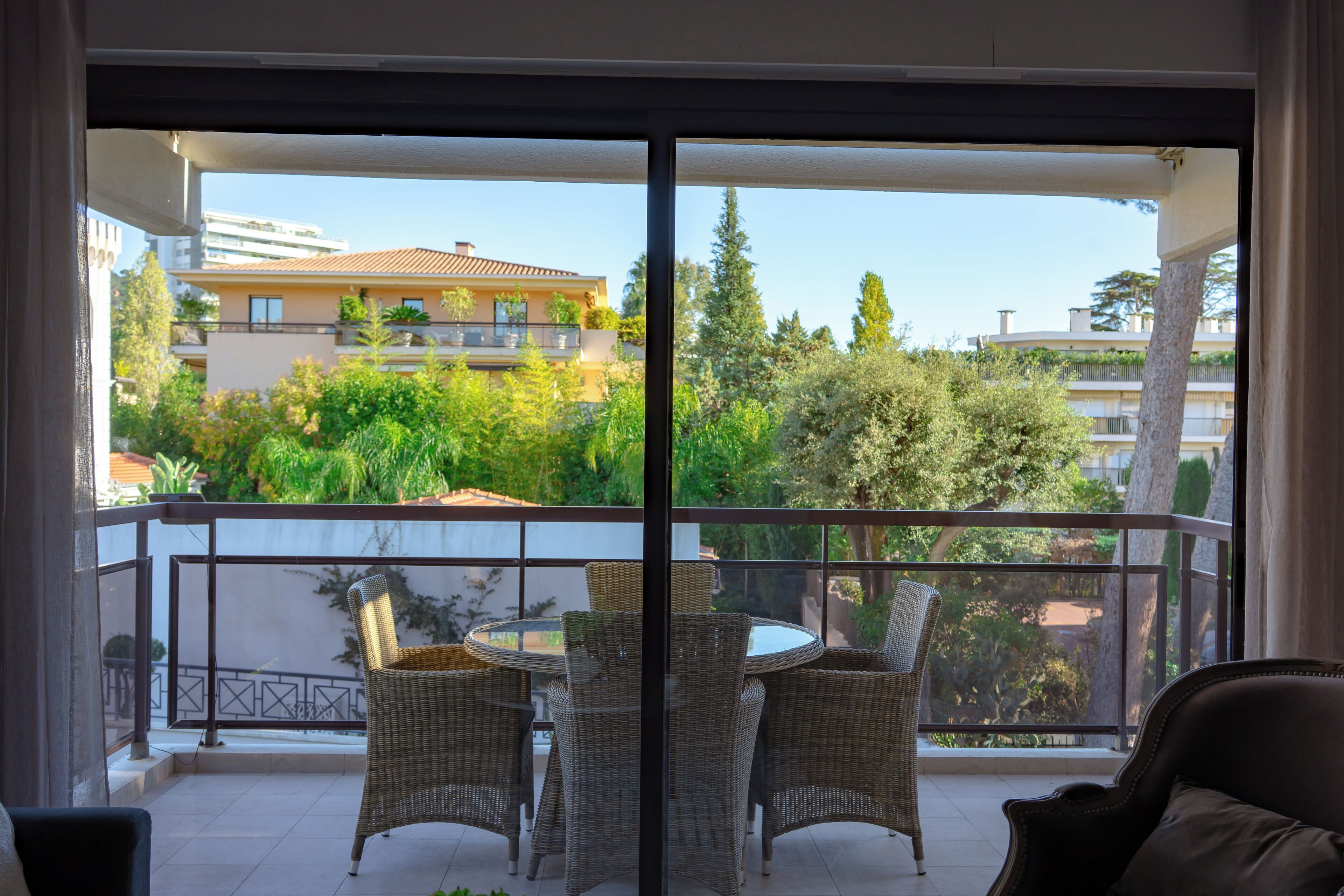 Varanda com cadeiras de vime e uma mesa, com vista para uma área residencial com árvores e edifícios.