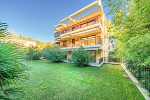 A multi-story residential building with balconies, a well-maintained lawn, and surrounding greenery.