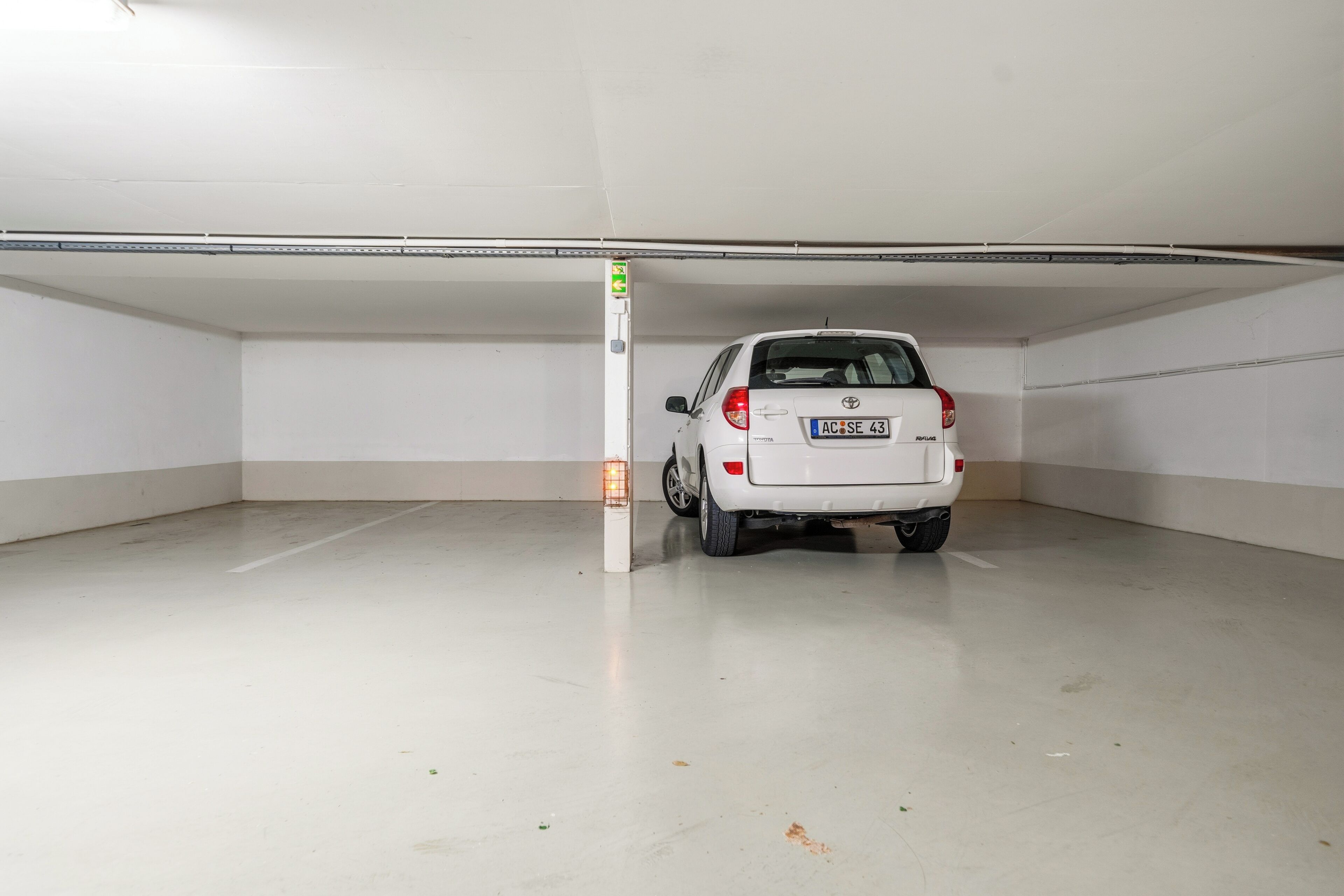 A white car parked in an empty parking garage with white walls and a concrete floor.