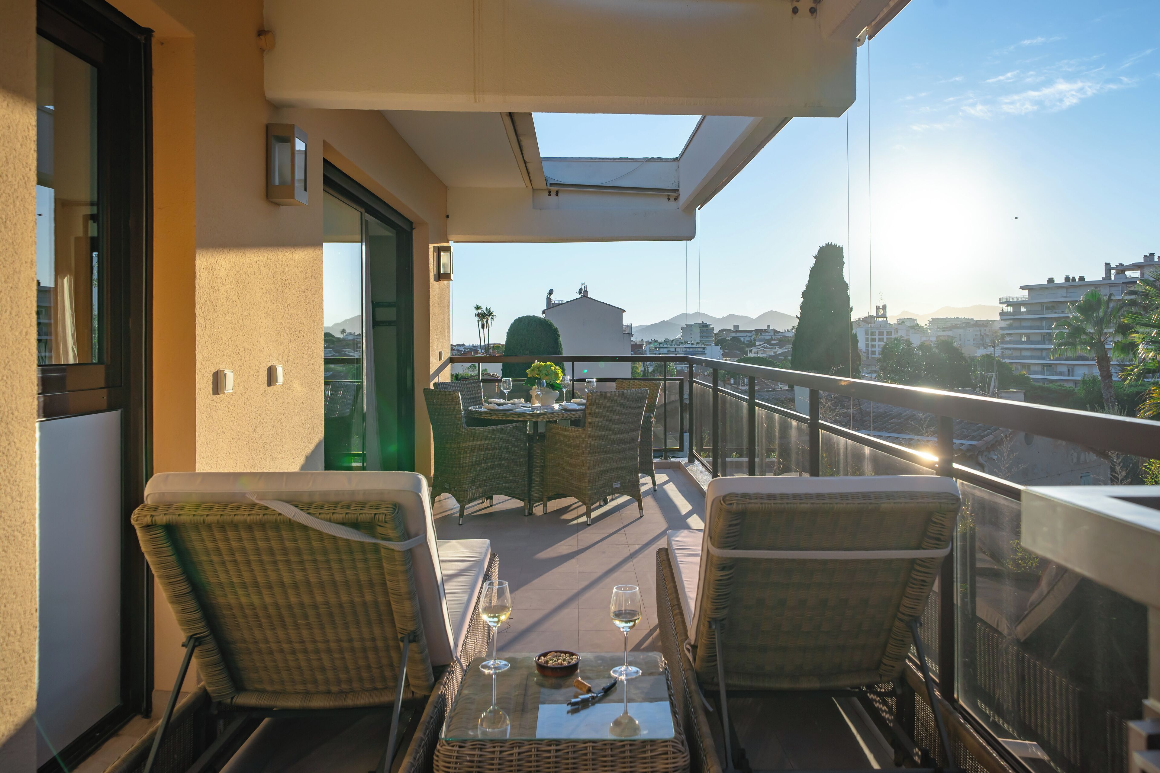 A balcony with wicker furniture, two glasses of white wine, and a table set for two.