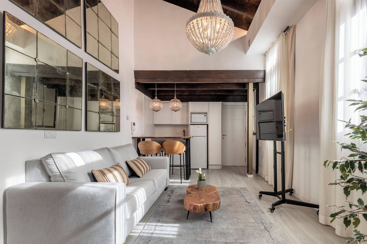 A modern living room with a grey sofa, wooden side tables, and a large chandelier.