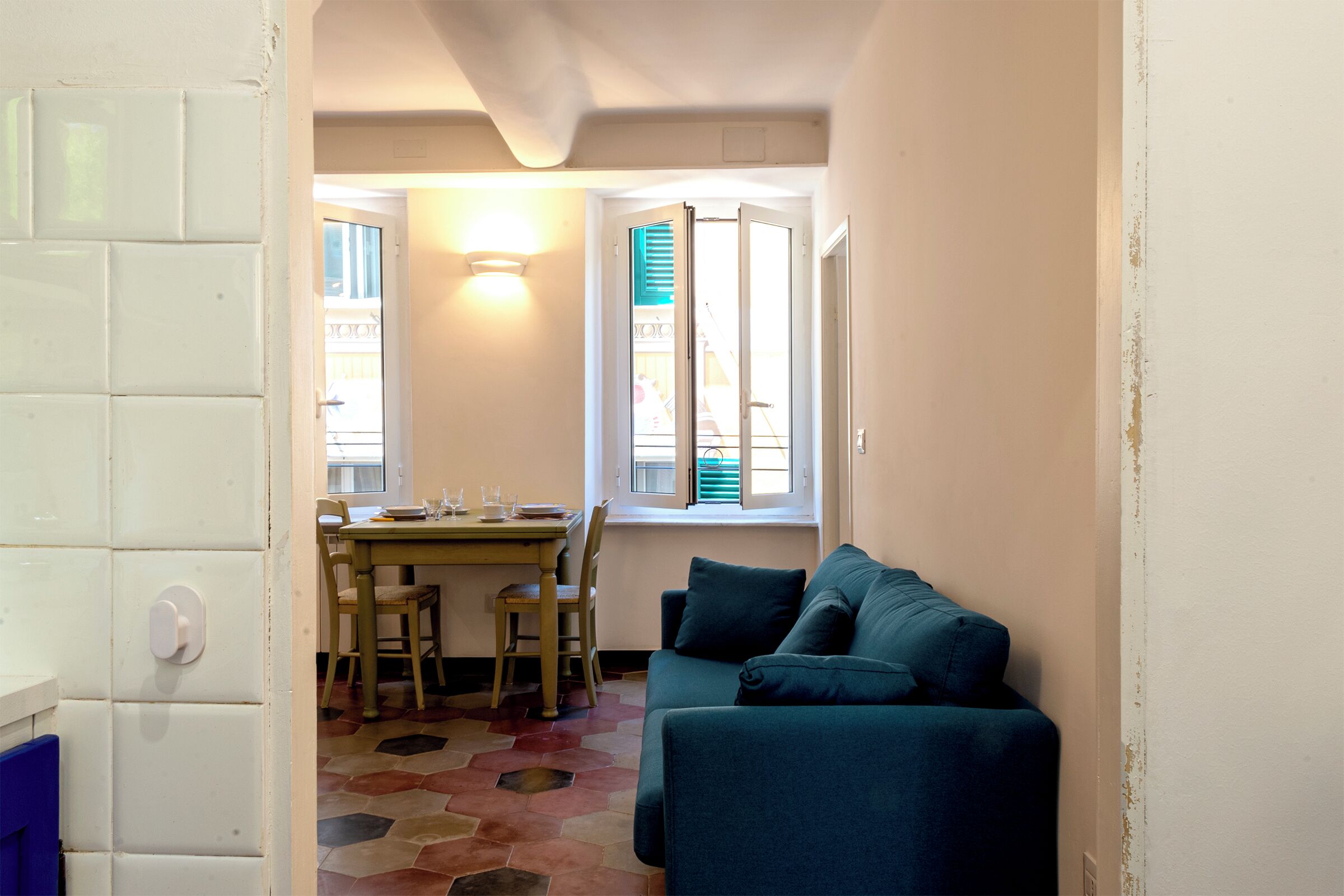 A room with a teal sofa, a dining table with chairs, and a window with shutters.
