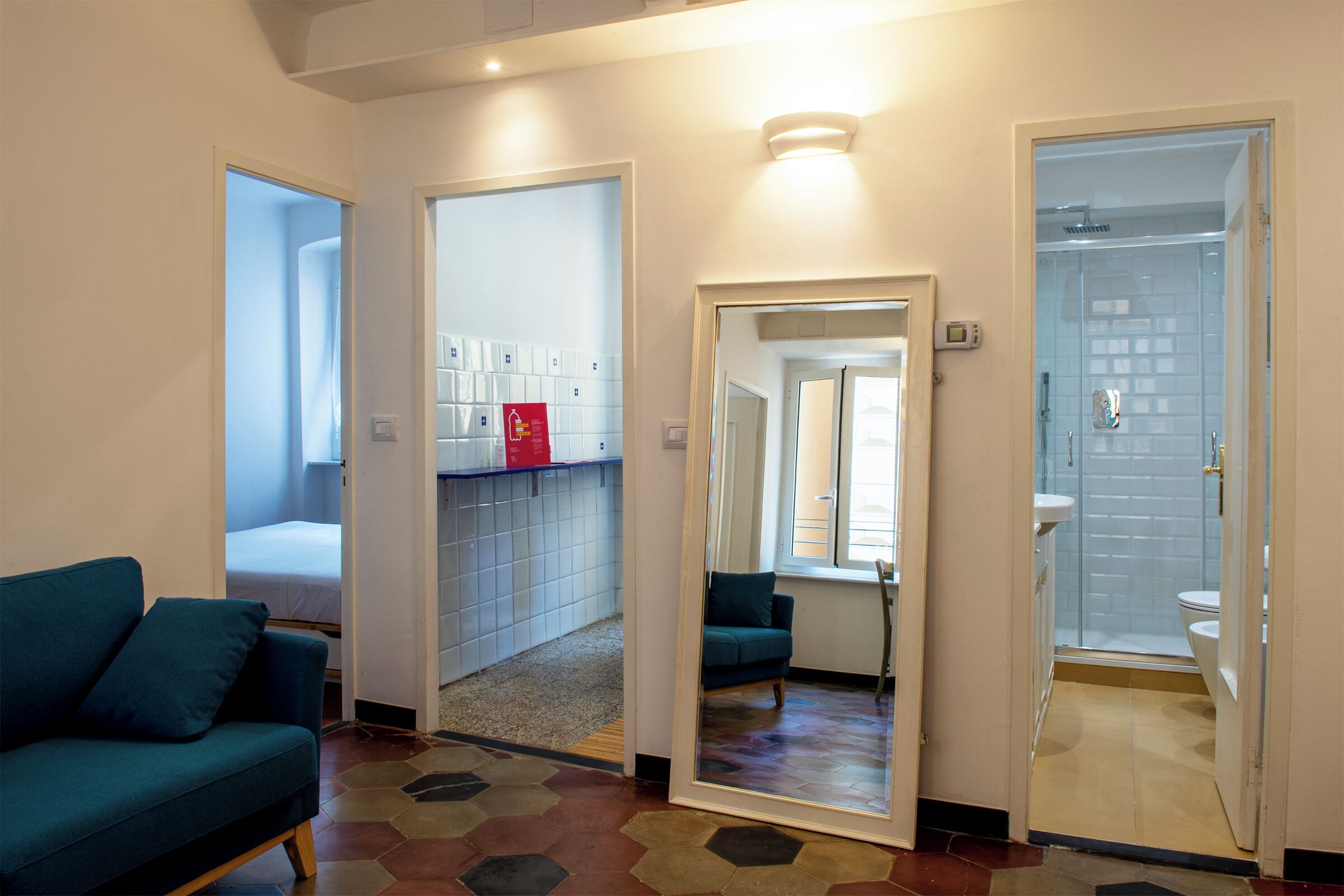 A hotel room with a bed, a sofa, a bathroom with a shower, and a mirror reflecting the room.