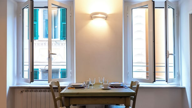 A dining table set with plates, glasses, and cutlery in a room with two windows, a radiator, and a light fixture. - Il Campanile by Wonderful Italy  (Camogli)