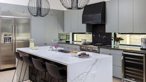 Een moderne keuken met een marmeren kookeiland, roestvrijstalen apparatuur en hanglampen.