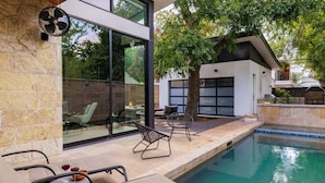 Een moderne buitenzwembadzone met ligbedden, een ventilator en een glazen patio.