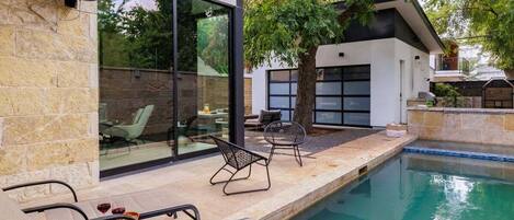 Een moderne buitenzwembadzone met ligbedden, een ventilator en een glazen patio.