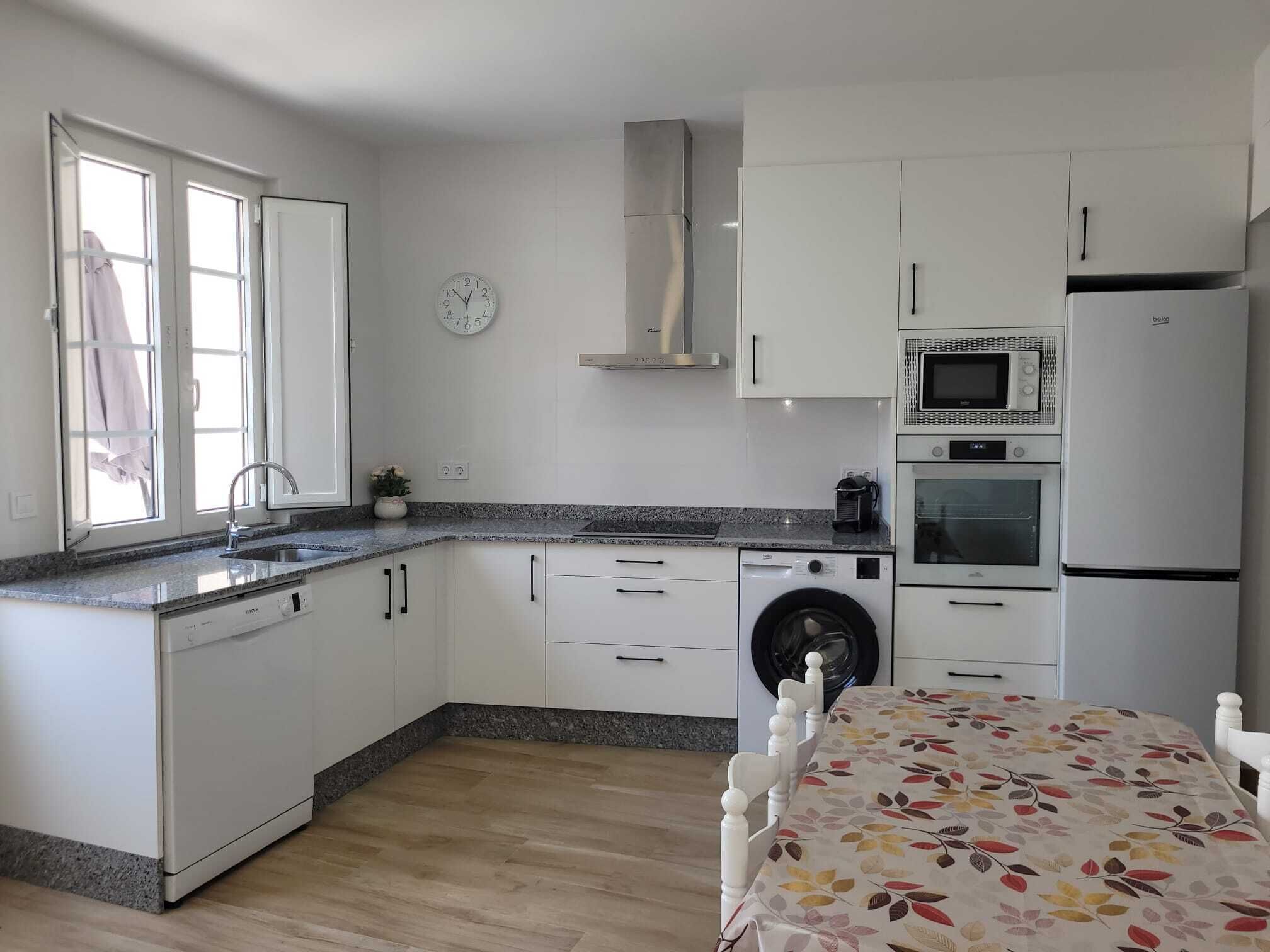 A compact kitchen with white cabinets, a built-in microwave, oven, and washing machine.