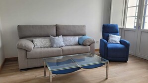 Una sala de estar con un sofá gris, un sillón azul y una mesa de centro de vidrio.
