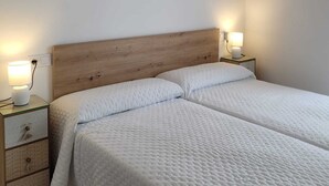 Un dormitorio con cabecera de madera, dos mesitas de noche con lámparas y una cama con ropa blanca.