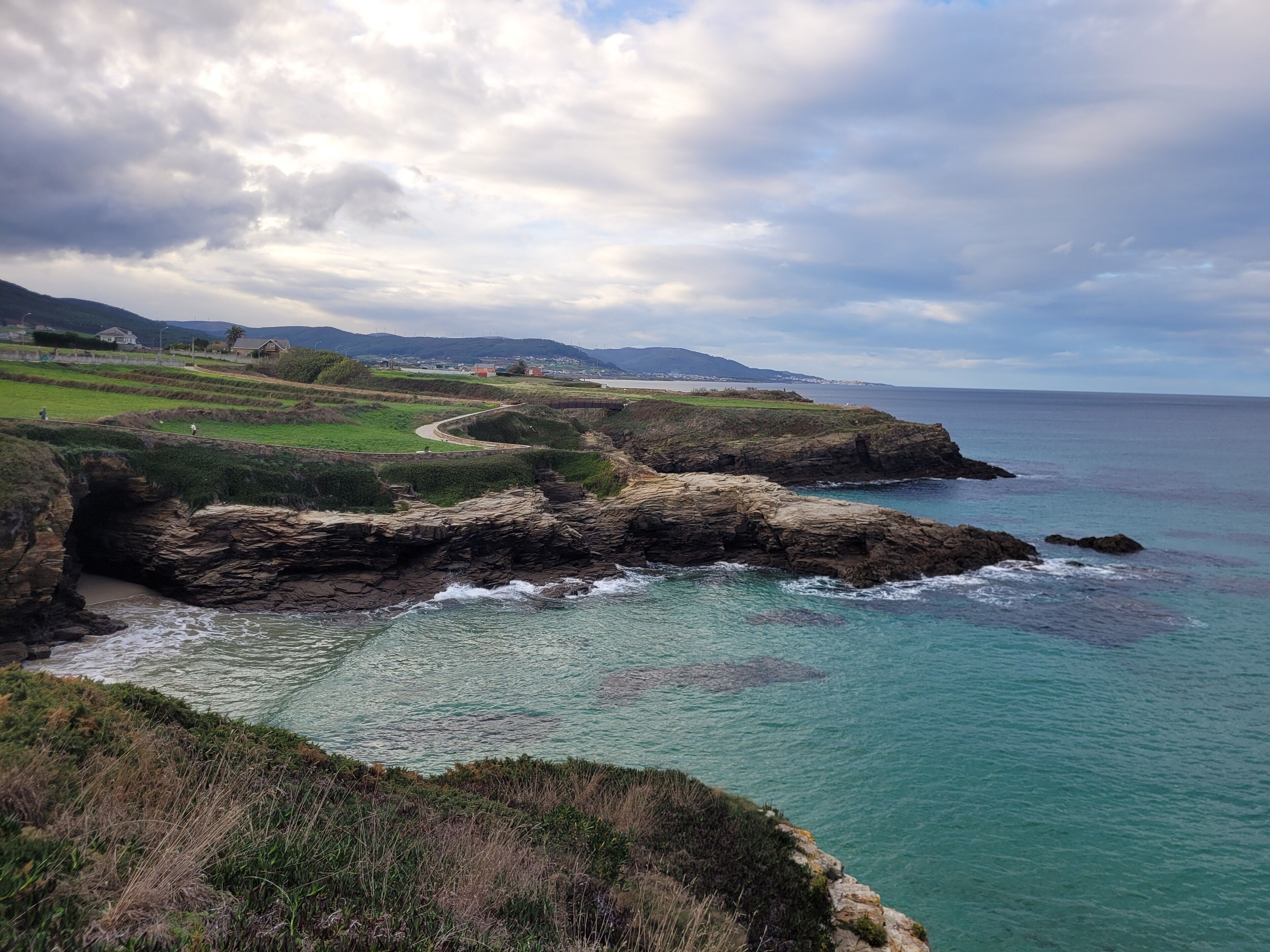 A coastal landscape with rocky cliffs, a winding path, and a view of the sea.